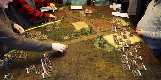 Tabletop surrounded by people playing miniatures wargame
